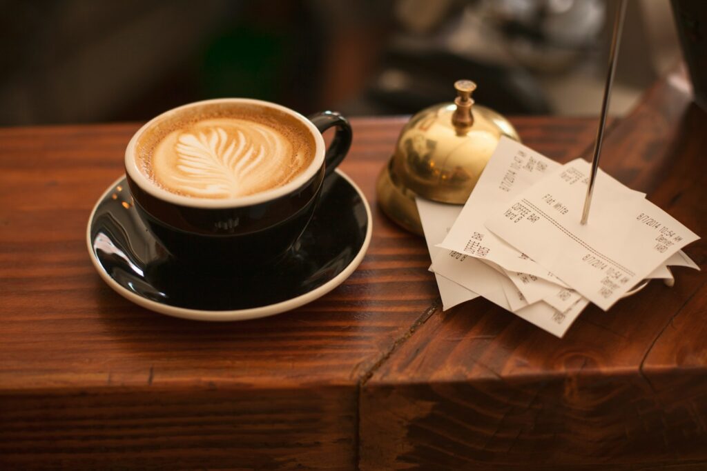 black ceramic cup with saucer and cappuccino on brown wooden surface with political receipts